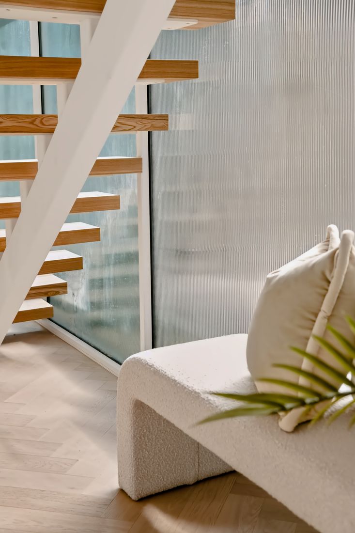 A staircase of pale timber treads with white stringers beside a full-height fluted glass partition