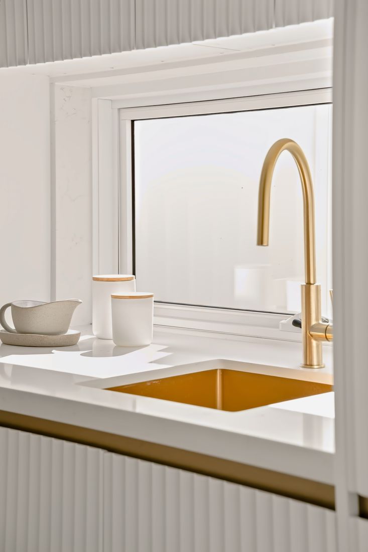 Brushed brass tap and sink set into a marble top against fluted white cabinetry