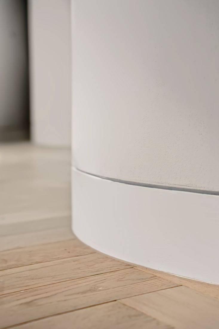 A curved white skirting meeting a herringbone oak floor with a crisp shadow line