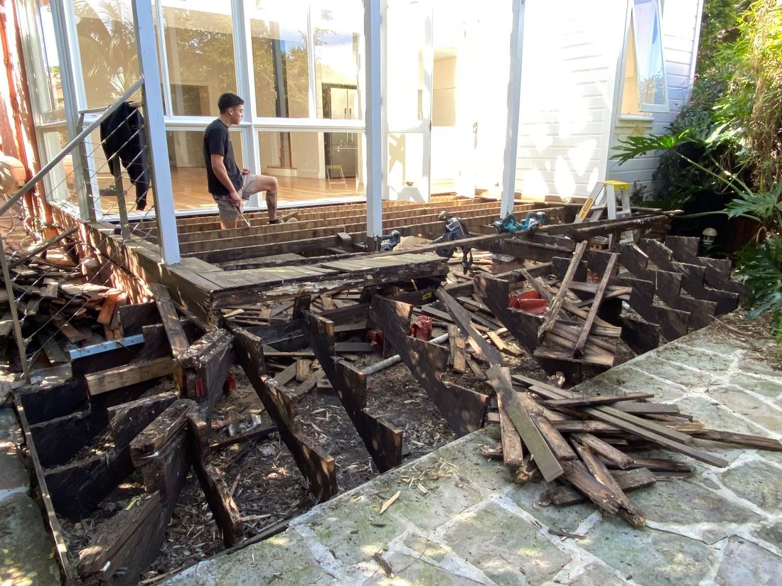 The old deck being pulled up, its boards and frame stacked on the paving