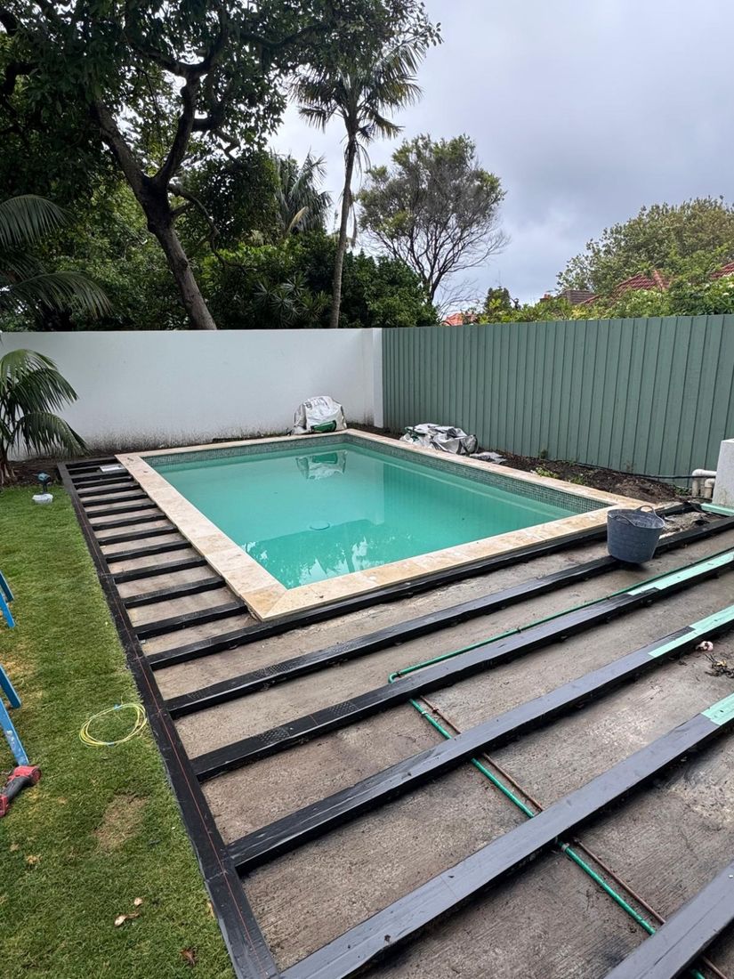 A low deck frame laid out on the ground beside the pool
