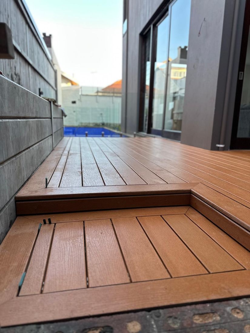 A low composite deck with a step-down platform in a narrow side courtyard, a pool beyond