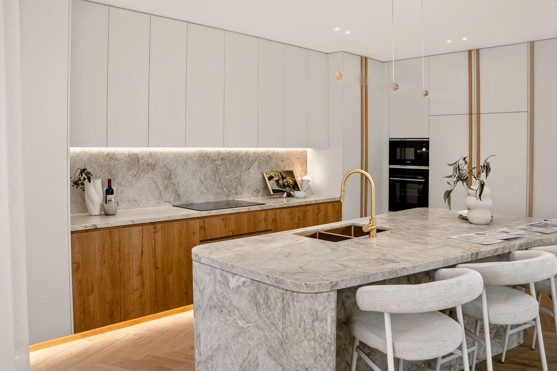 A kitchen run of matte white overheads above oak under-bench joinery, marble splashback and island