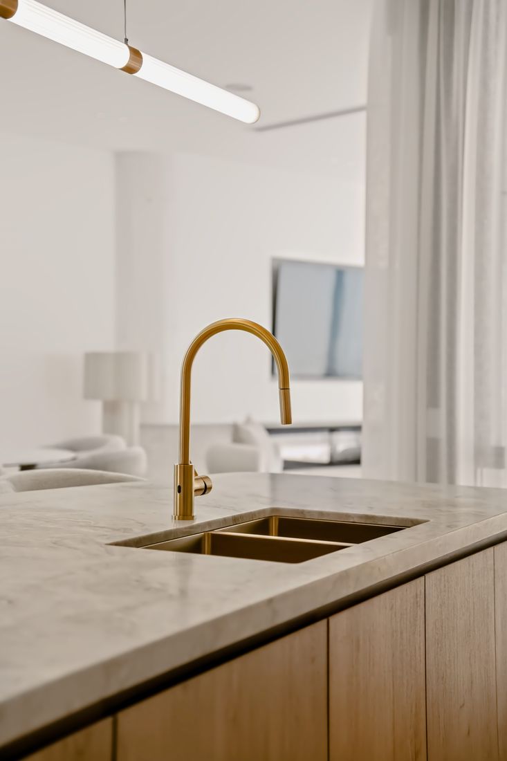 A brushed brass mixer and integrated double basin set into a marble island with oak cabinetry below