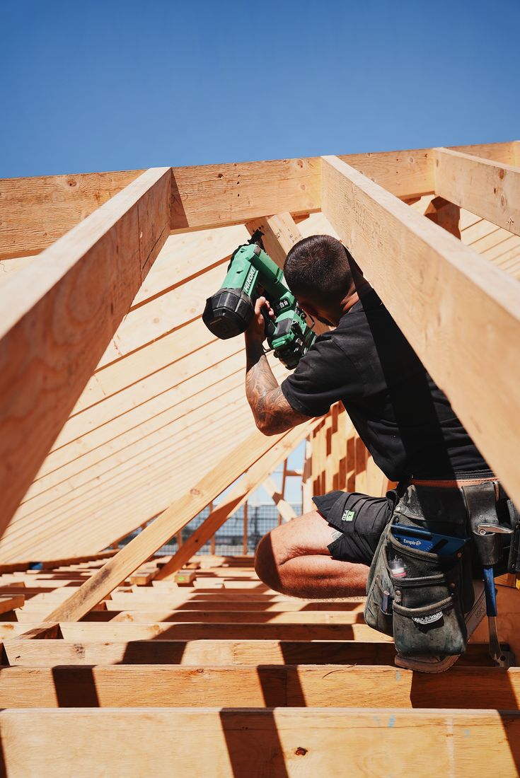A carpenter fixing a rafter with a nail gun inside the roof frame