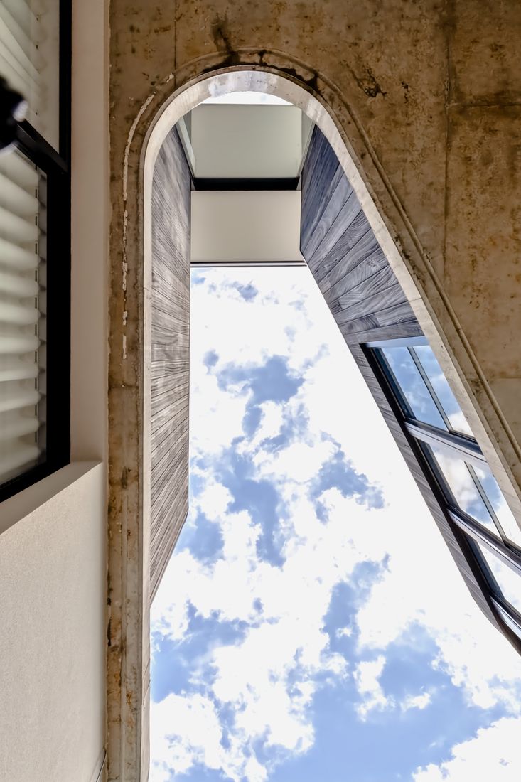 Low-angle view up between two volumes — charred timber cladding, a concrete edge sweeping overhead and a sliver of blue sky