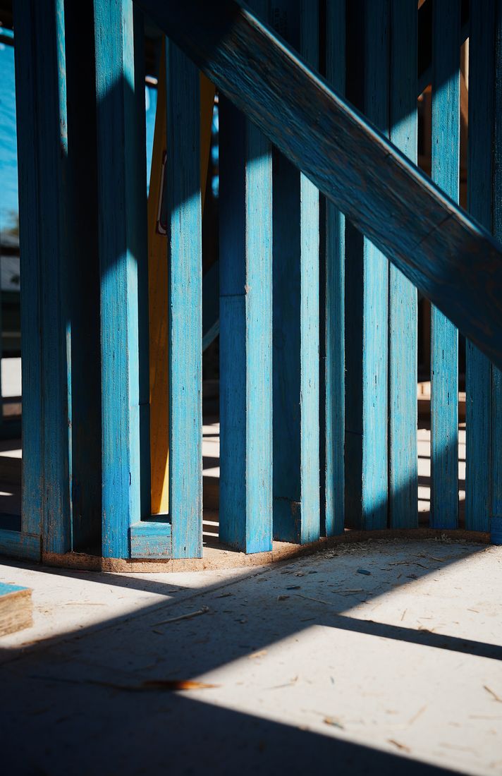 Close low-angle view of blue-stained timber wall studs with a diagonal brace, resting on a pale floor plate in hard sunlight