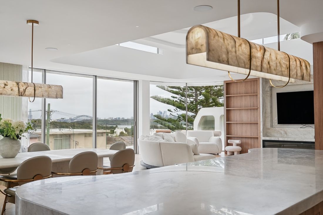 A stone island in the foreground, the living and dining area beyond, and Sydney Harbour and the city skyline through full-height glazing