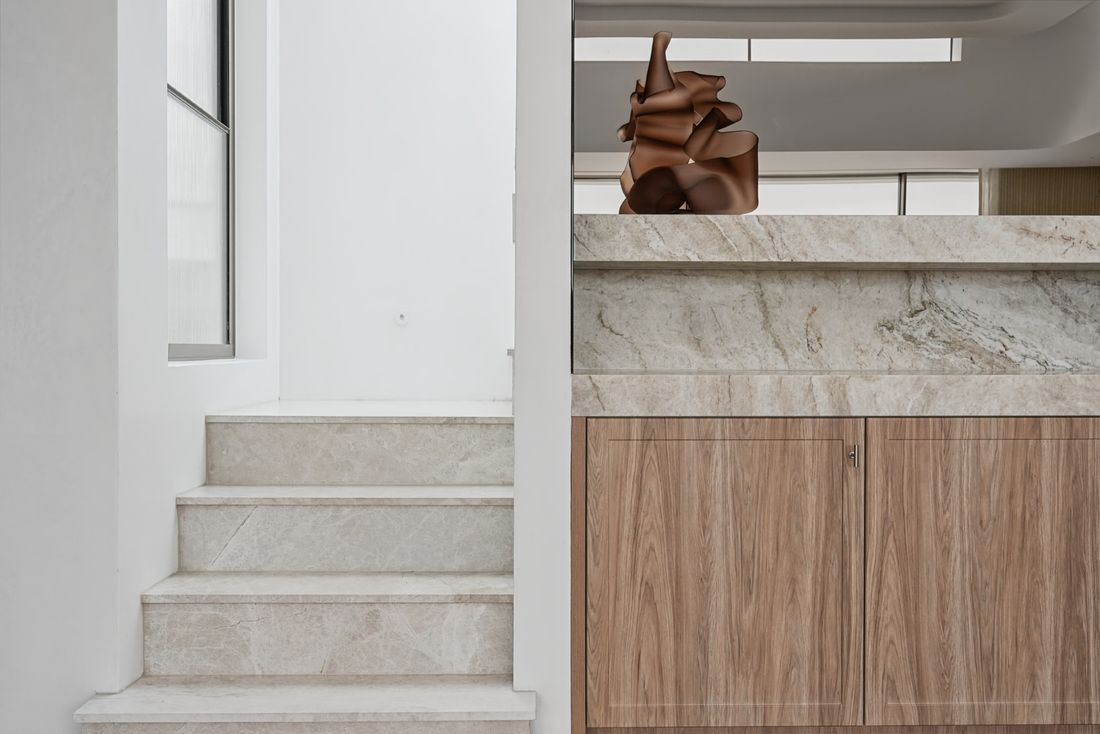 Light stone stair treads beside a timber-veneer cabinet with a stone top and a sculpture on it