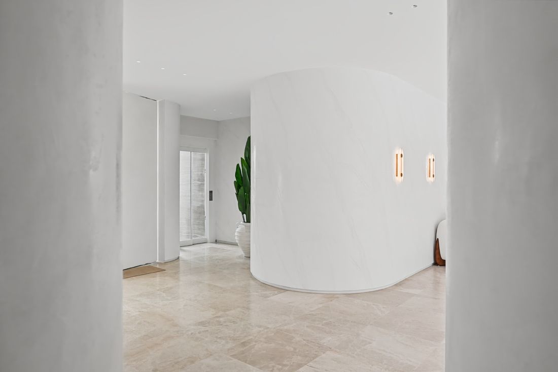 A curved wall in white specialty render with two wall lights, a marble floor and a potted plant