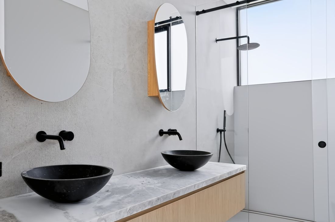 A floating oak vanity with twin black vessel basins beneath a marble top
