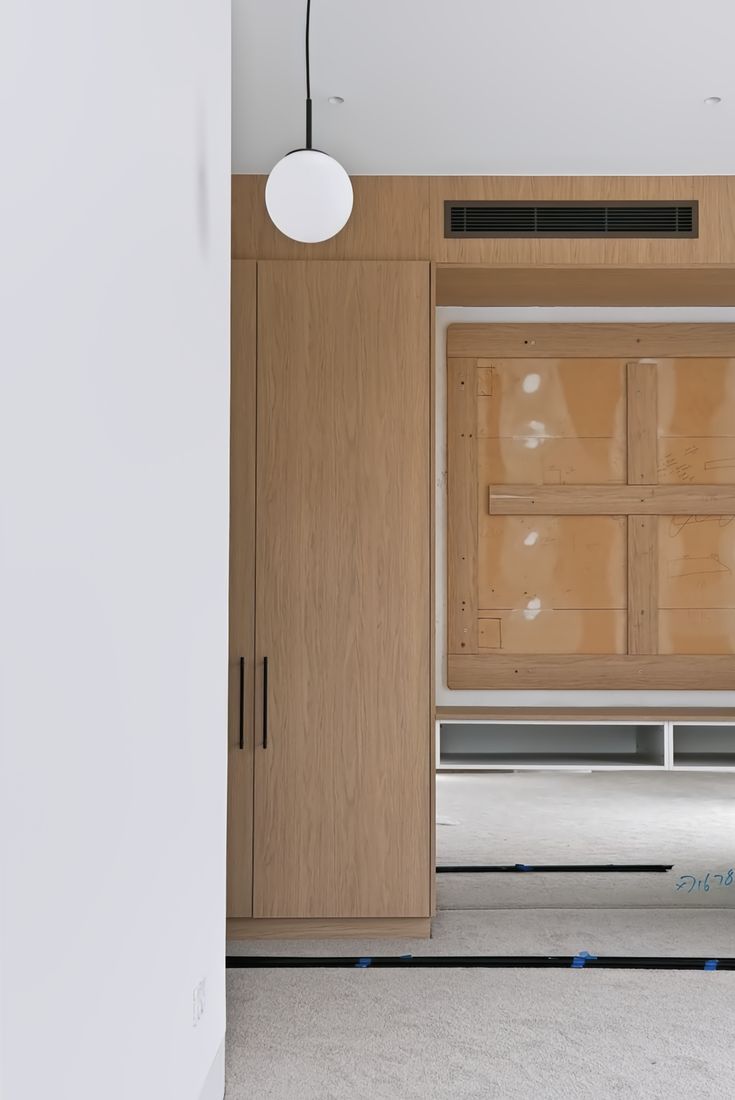 A wall-hung oak cabinet unit with black pulls, a black vent grille and a globe wall sconce above a white desk