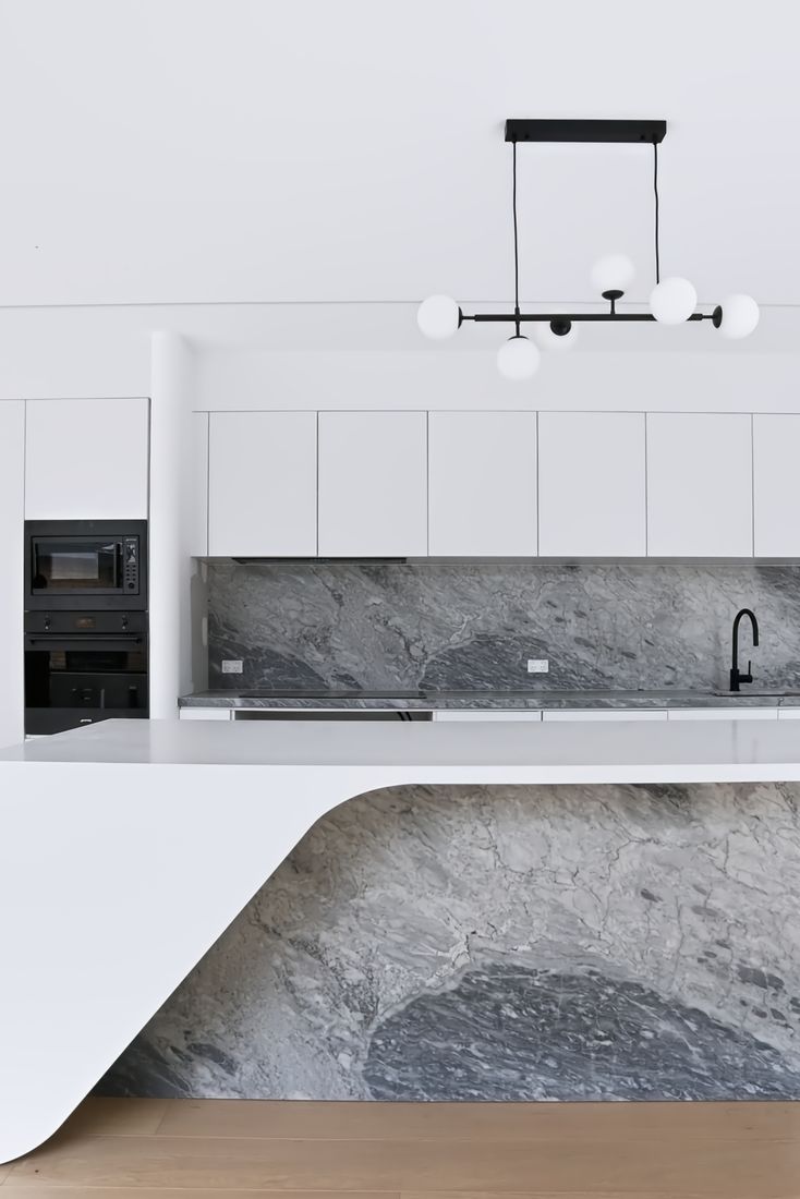 Top-down view of a veined marble counter and splashback in white cabinetry, with a black five-globe pendant and black tap