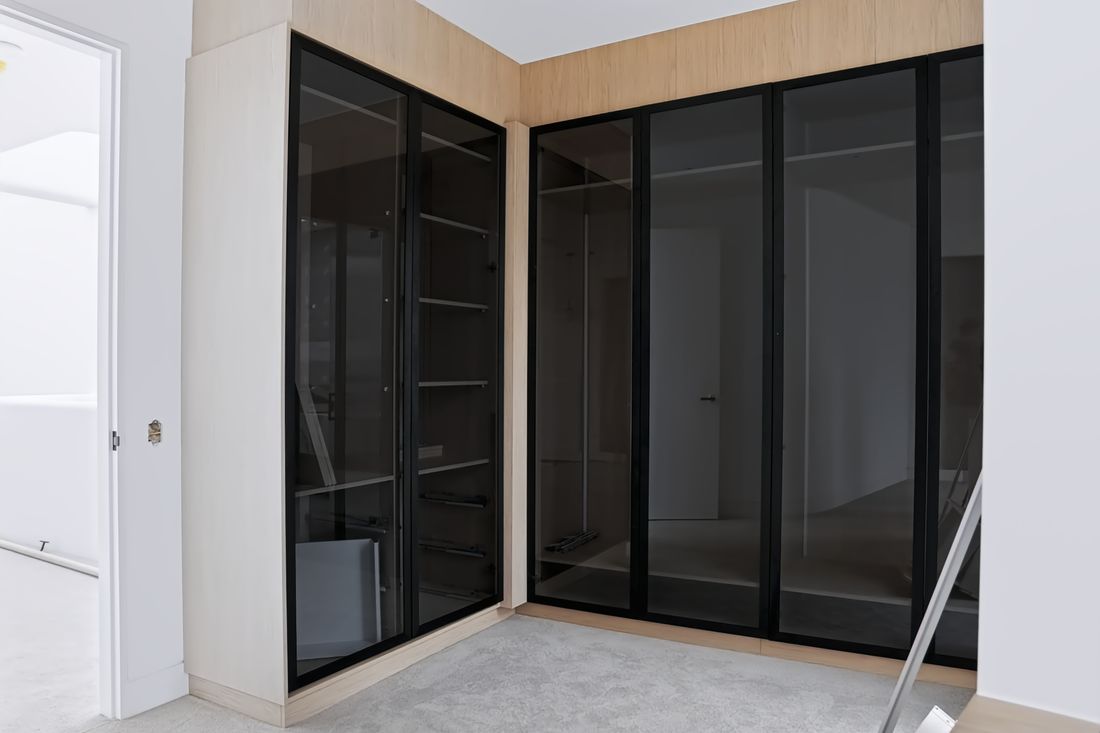 A corner closet in oak with slim black-framed smoked glass doors opening to shelves and hanging space