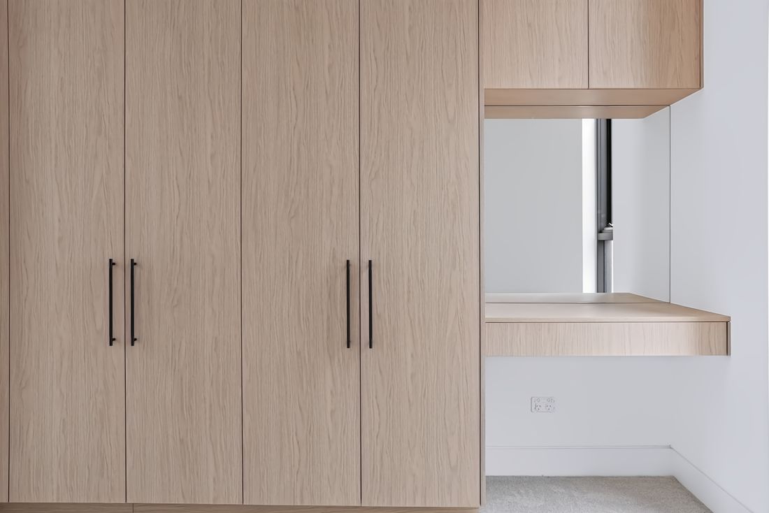 Light oak wardrobes beside a recessed vanity nook with a mirror and floating shelf