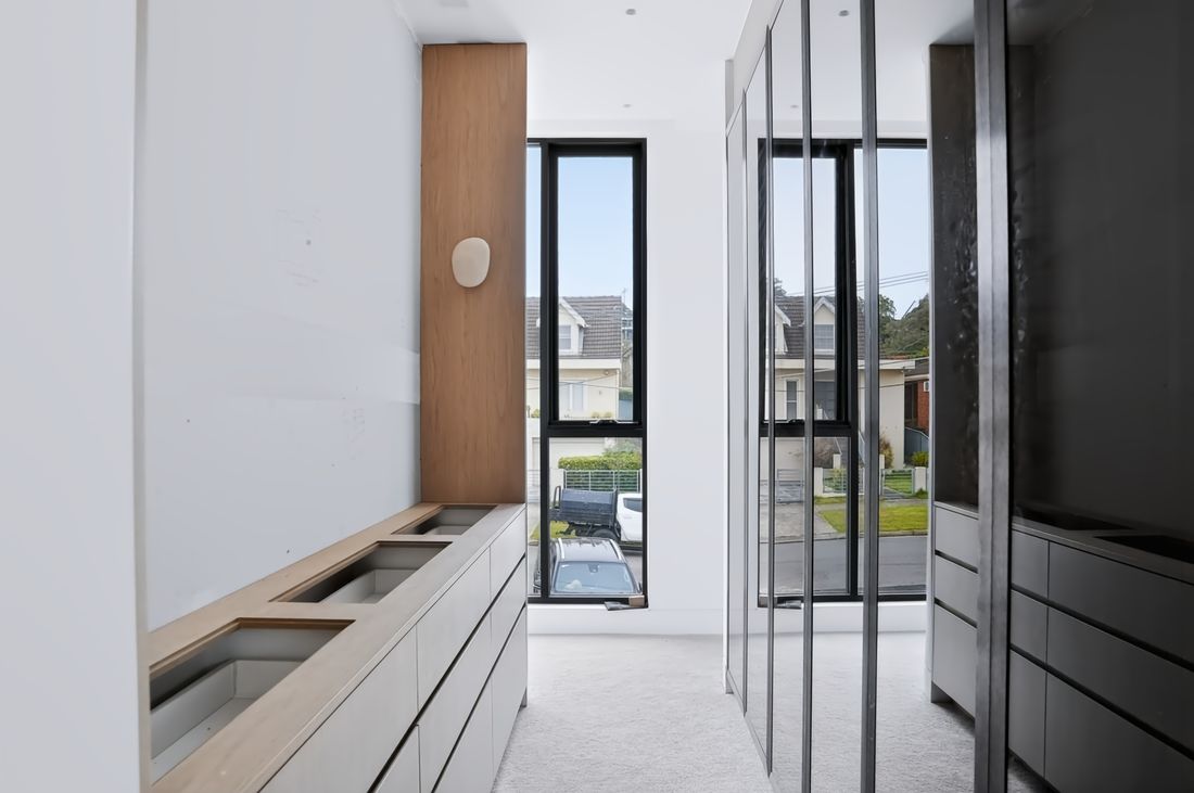A dressing corridor between oak and grey cabinetry and tinted glass wardrobes, closing on a tall window